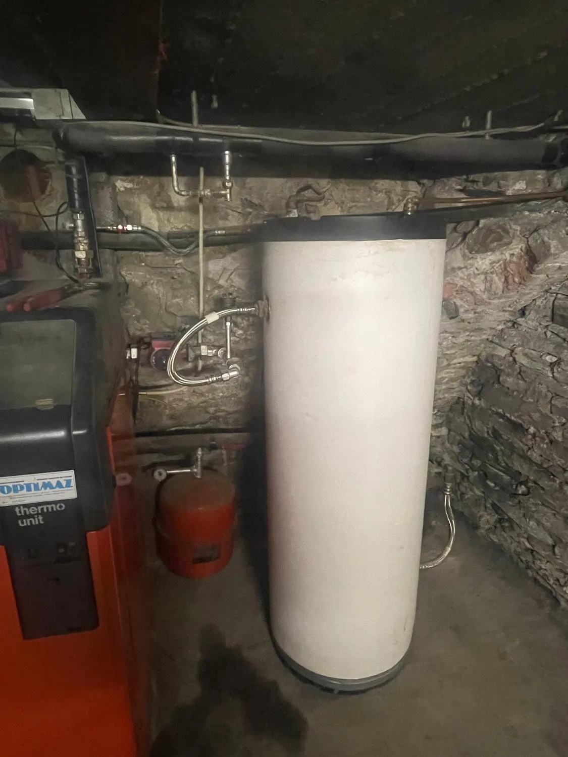Ancien boiler à côté de la chaudière avant son remplacement, avec une trace d'eau au sol