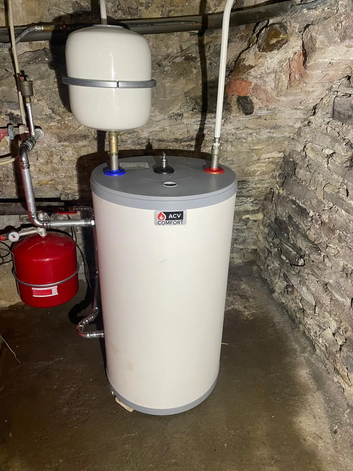 Vue d'ensemble du boiler ACV Comfort installé et raccordé en tuyauterie inox dans une cave en pierre