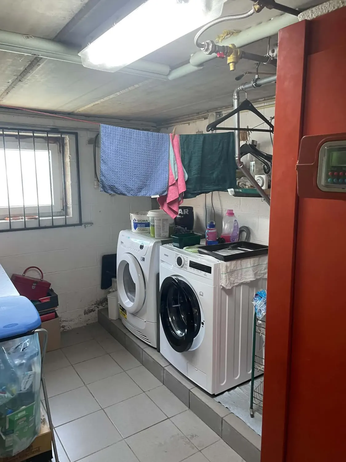 Vue d'ensemble de la buanderie avant les travaux, avec lave-linge et sèche-linge sur un socle