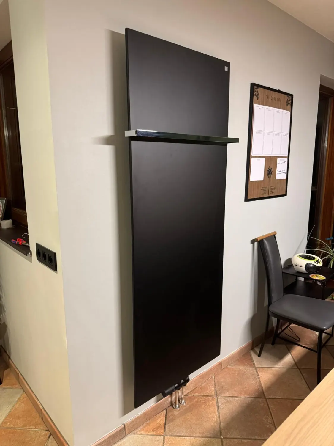 Radiateur design vertical noir mat avec porte-serviette chromé, fixé au mur d'une pièce de vie