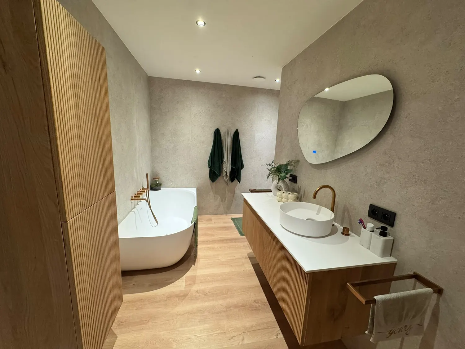 Salle de bain rénovée avec baignoire îlot, meuble vasque en bois et robinetterie dorée