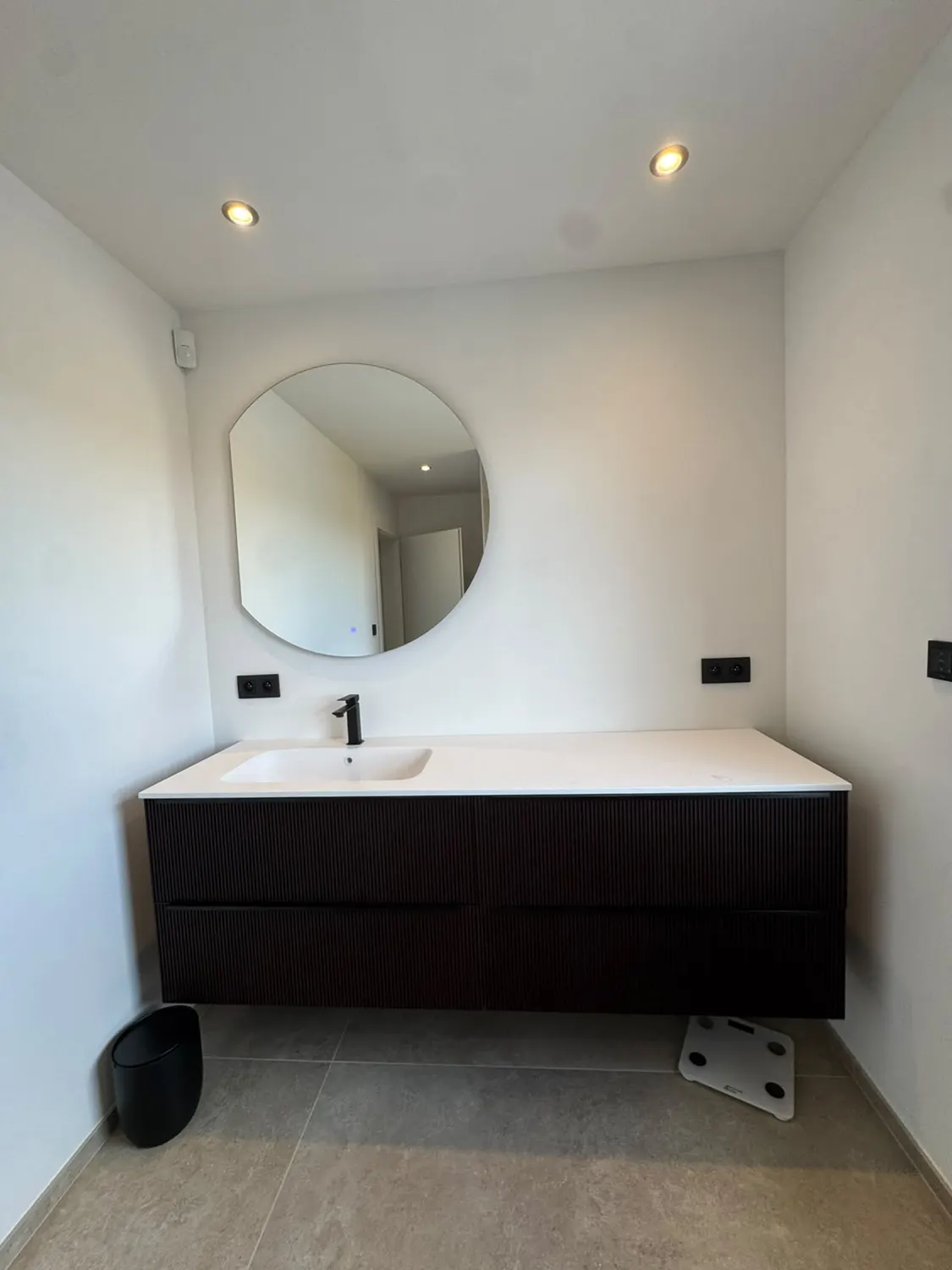 Meuble vasque noir strié et miroir rond dans une salle de bain contemporaine