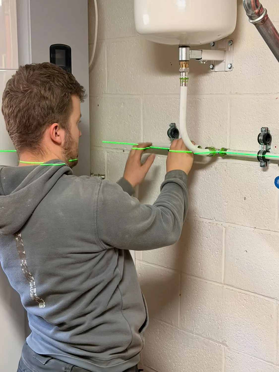 Technicien posant une tuyauterie multicouche à l'aide d'un niveau laser sous un vase d'expansion