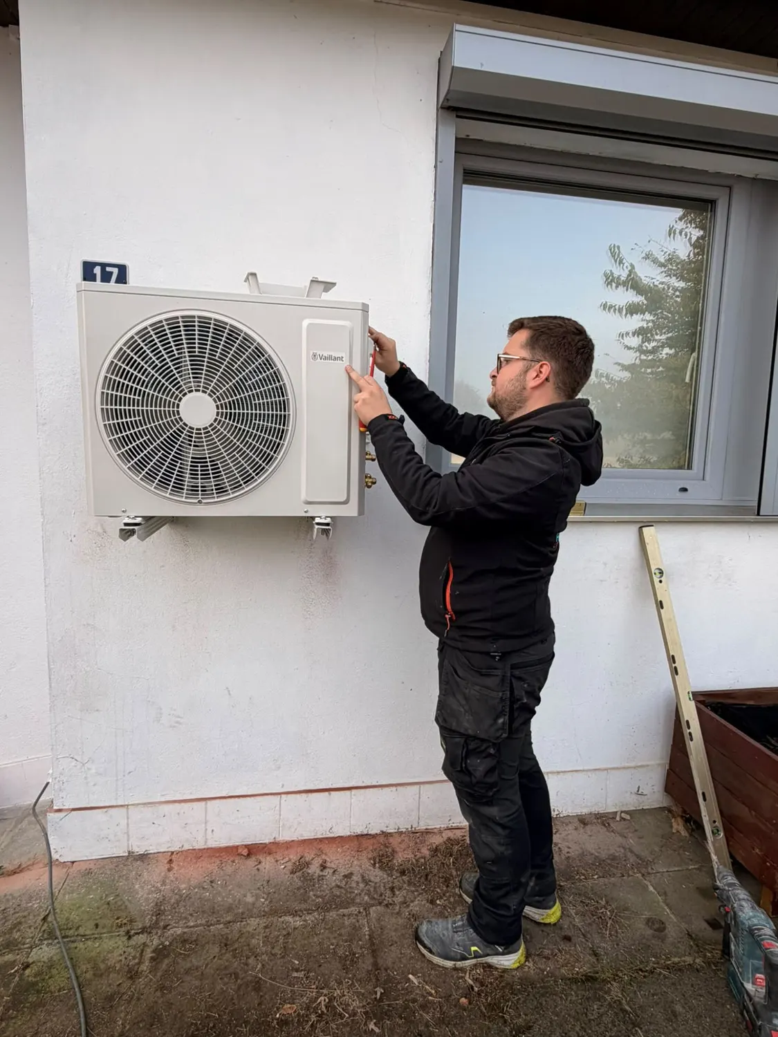 Technicien d'ABL Chauffage réglant l'unité extérieure fixée au mur de la façade