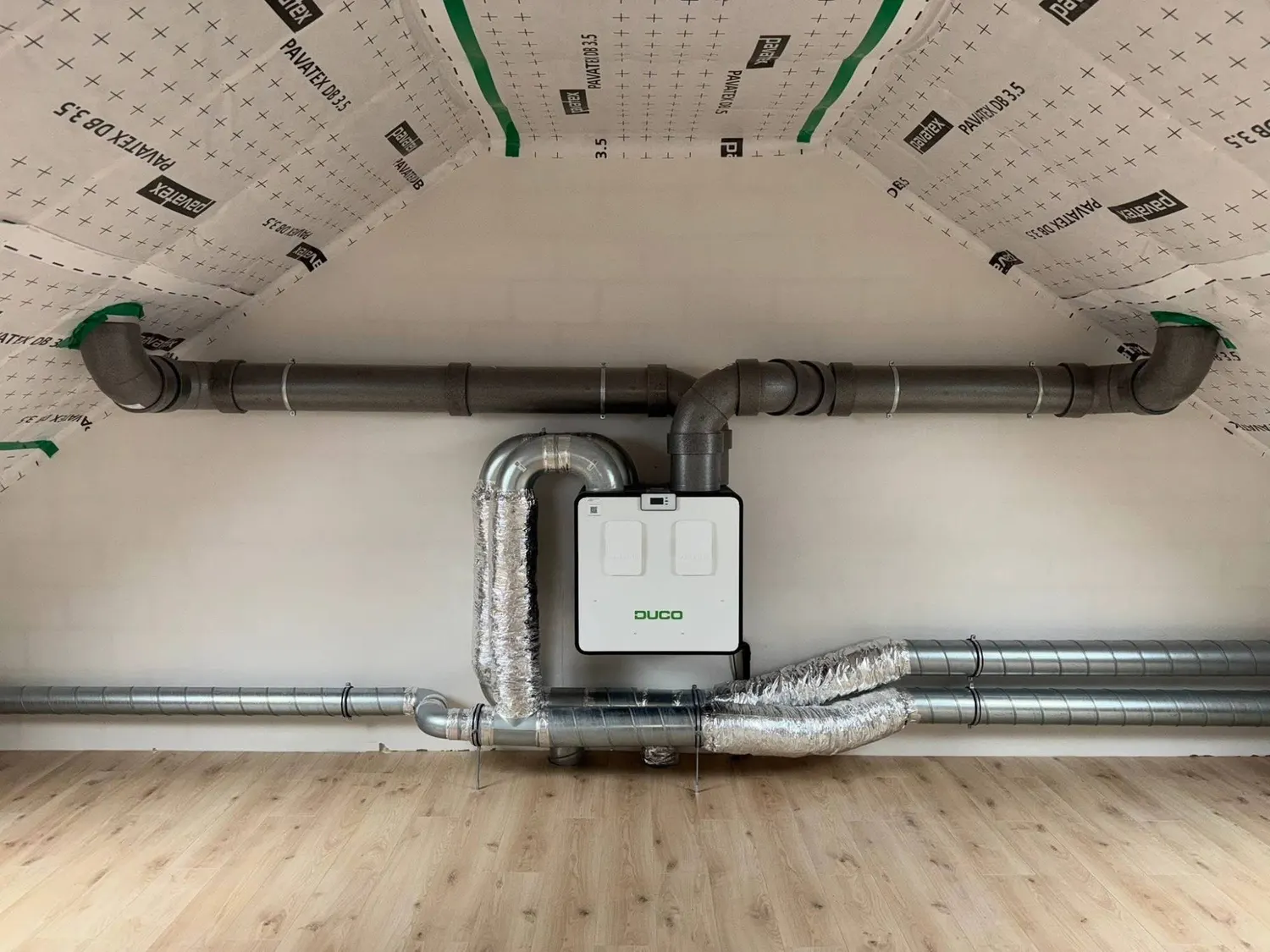 Unité de ventilation double flux Duco suspendue sous les combles, avec gaines spiralées et coudes isolés